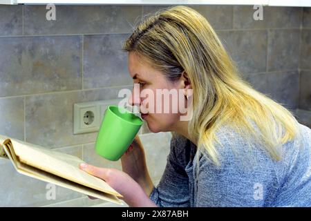 Leaning on the table, a woman drinks tea and reads a book.. High quality photo Stock Photo