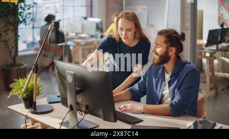 Team of Two Young Entrepreneurs Talking, Discussing Growth Strategy at a Desk with Computers. Stylish Businesspeople Work on an Investment and Marketing Project in a Creative Agency. Stock Photo