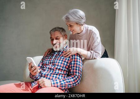 Mature woman leaning on man video calling through smart phone at home Stock Photo