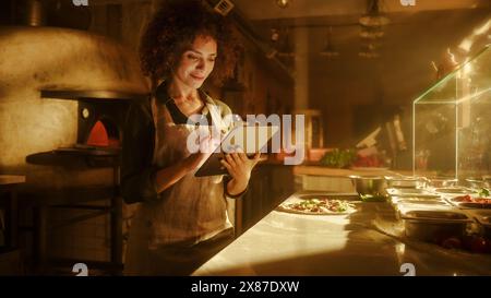 In Restaurant: Beautiful Female Chef Using Laptop Computer. Authentic Pizza Place Cooking Delicious Organic Eco Food. Bi-racial Female Entrepreneur Working on Online Order, Small Business Family Shop Stock Photo