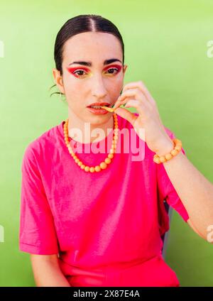 Fashionable woman eating french fries sitting against green background Stock Photo