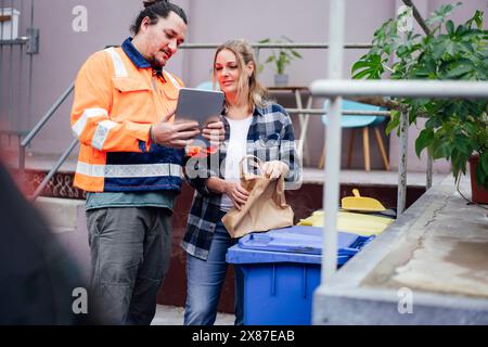 Sanitation worker sharing tablet PC with woman standing by garbage bins Stock Photo