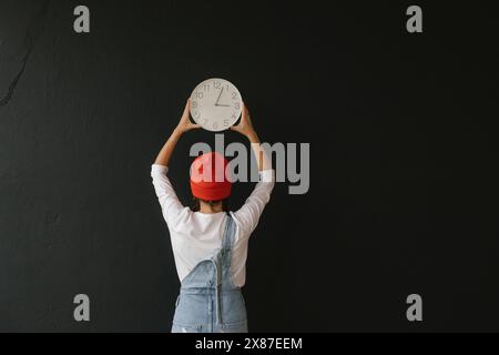 Woman holding wall clock against black background Stock Photo