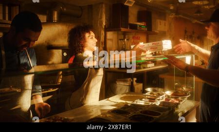 In Small Business Family Restaurant: Professional Couple of Chefs Preparing Pizza, Traditional Family Recipe, Giving Boxes to a Happy Customer. Authentic Sunny Pizzeria, Cooking Delicious Organic Food Stock Photo