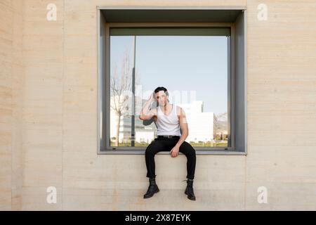 Handsome young man sitting on window of building Stock Photo