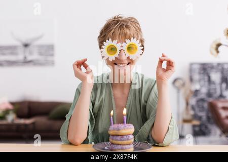 Happy woman in floral sunglasses with doughnuts on table at home Stock Photo