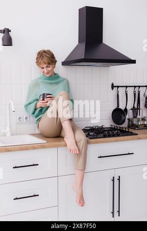 Woman sitting on kitchen counter at home Stock Photo