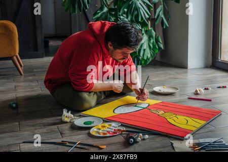 Painter painting on canvas sitting cross-legged on floor at home Stock Photo