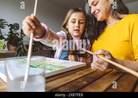 Grandmother and granddaughter painting together at table at home Stock Photo