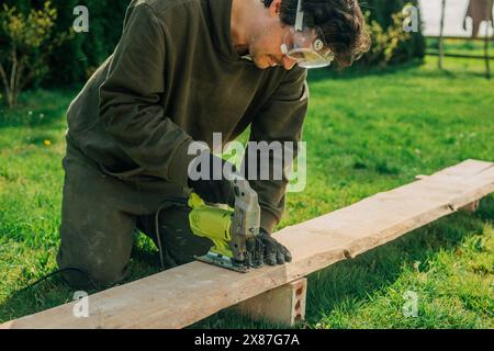 Man cutting plank with electric saw in backyard Stock Photo