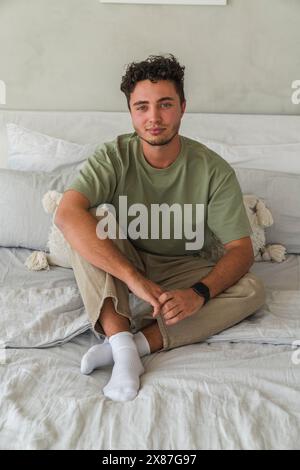 Smiling young man sitting on bed at home Stock Photo