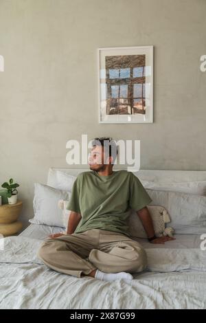 Young man sitting on bed in bedroom at home Stock Photo