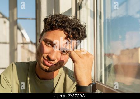Smiling young man sitting near window Stock Photo