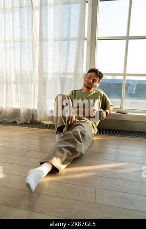 Young man holding coffee cup and sitting near window at home Stock Photo