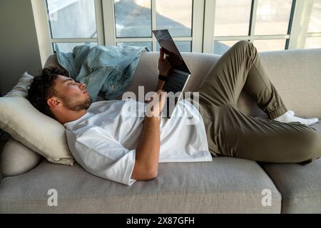 Young man lying on sofa and using laptop at home Stock Photo