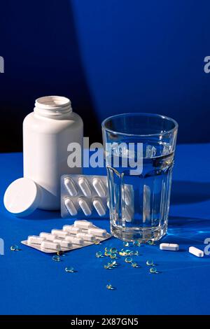 Glass of water near pill bottle on blue background Stock Photo