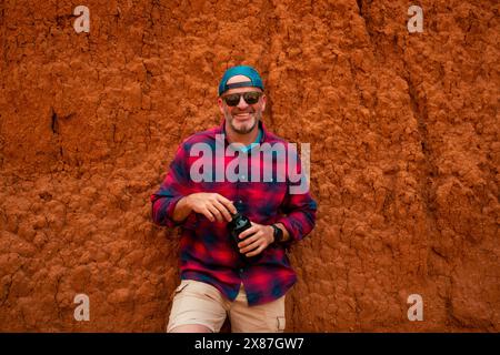 Smiling mature man with water bottle leaning on red rock formation at canyon Stock Photo