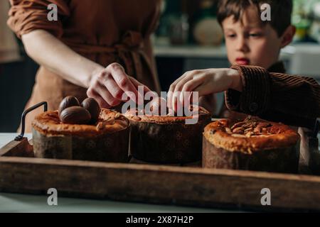 Boy and mother decorating Easter cakes with chocolate eggs in kitchen Stock Photo