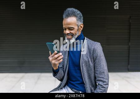 Smiling mature businessman using mobile phone in front of black wall Stock Photo