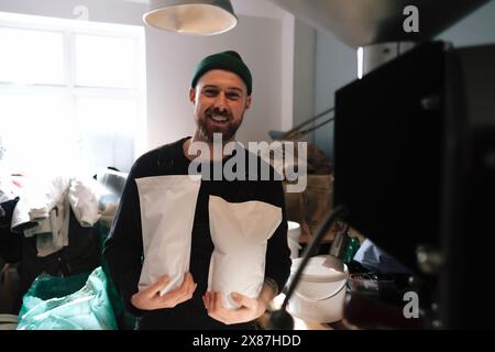 Smiling coffee roaster holding packed paper bags of coffee beans in factory Stock Photo