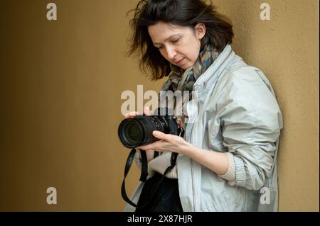 Woman leaning on yellow wall holding camera Stock Photo