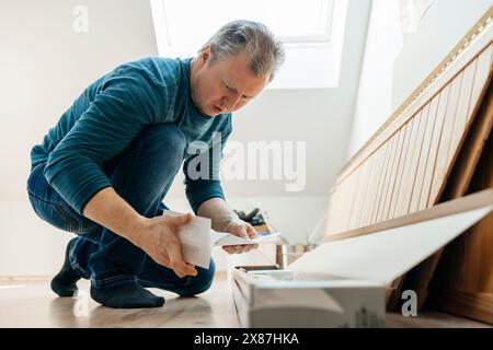Man reading instruction manual kneeling on floor at home Stock Photo