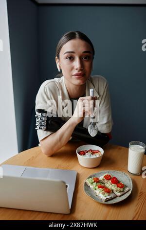 Young woman with bionic arm eating breakfast at table Stock Photo