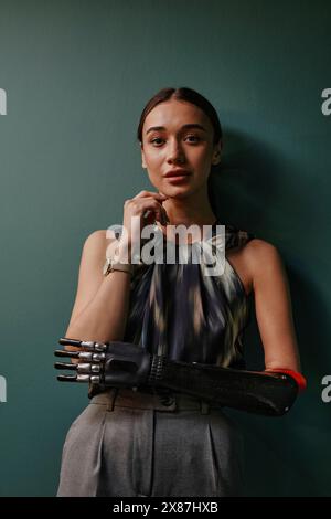 Confident woman with black bionic arm leaning on green wall Stock Photo