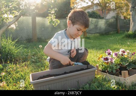 Boy digging soil from pot using shovel in garden Stock Photo