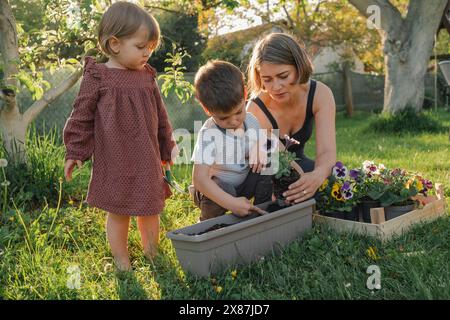 Mother assisting children potting plants in garden Stock Photo