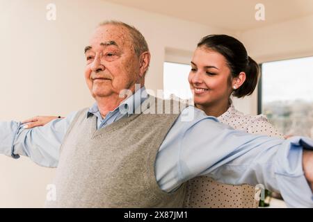 Smiling young doctor helping senior man with exercising at nursing home Stock Photo