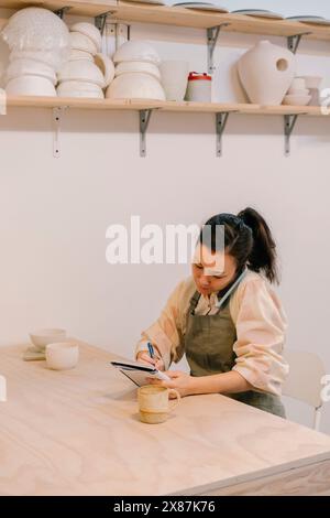 Craftsperson talking through smart phone and writing in diary at workshop Stock Photo