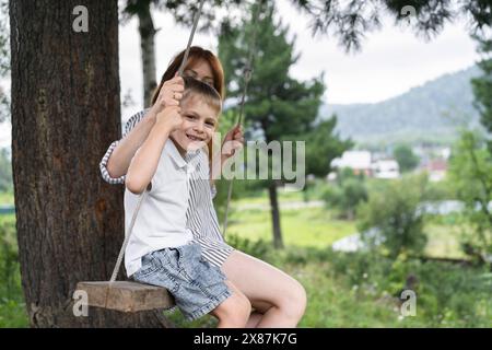 Happy boy sitting on swing with mother Stock Photo