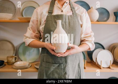 Potter standing with ceramic vase at workplace Stock Photo