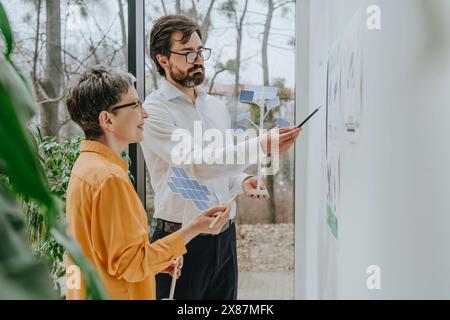 Smiling businesswoman with colleague explaining solar panels project in office Stock Photo