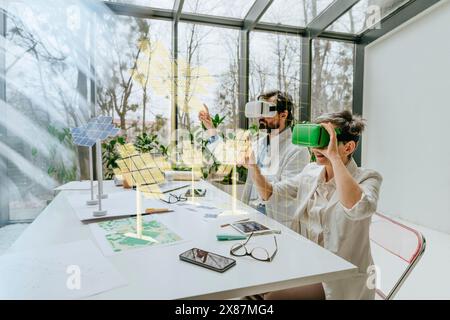 Engineers wearing virtual reality simulators and working on solar panels project at desk in office Stock Photo