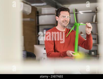 Smiling engineer examining green wind turbine model at office Stock Photo