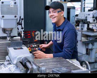 Happy apprentice operating CNC machine at factory Stock Photo