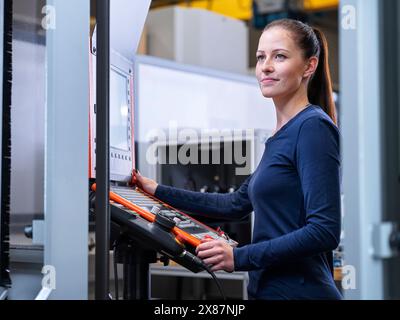 Smiling engineer standing near CNC machine panel at factory Stock Photo