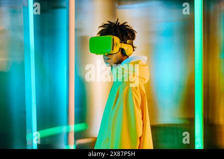 Young man in yellow jacket standing in front of illuminated wall Stock Photo