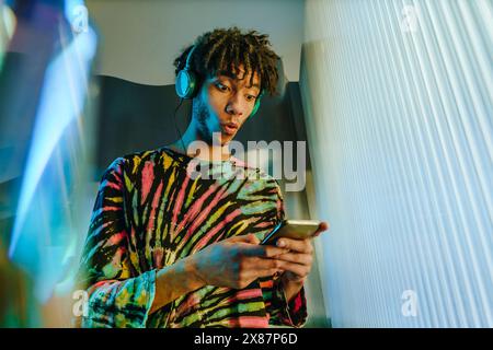 Surprised man holding smart phone near illuminated wall Stock Photo