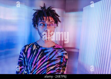 Thoughtful young man in sunglasses near illuminated wall Stock Photo