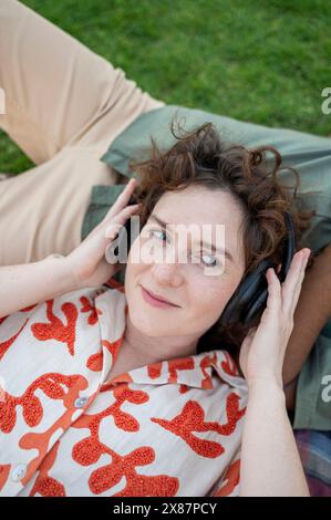 Smiling woman listening to music through wireless headphones and lying down on boyfriend Stock Photo