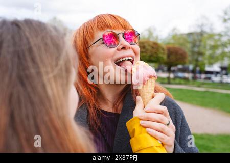 Girl feeding ice cream to mother at park Stock Photo