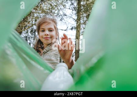 Smiling girl putting plastic bottle in garbage bag at forest Stock Photo