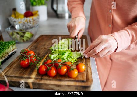Hands of woman cutting vegetables on wooden board in kitchen at home Stock Photo