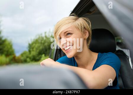 Happy young woman looking out through window sitting in car Stock Photo