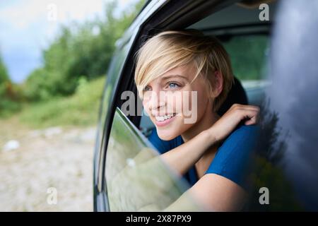 Smiling young woman looking out through window sitting in car Stock Photo