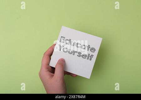 A hand holding a piece of paper with the words educate yourself written on it Stock Photo