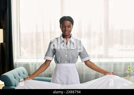 Minimal front view portrait of young African American woman making bed in luxury hotel room standing against window copy space Stock Photo